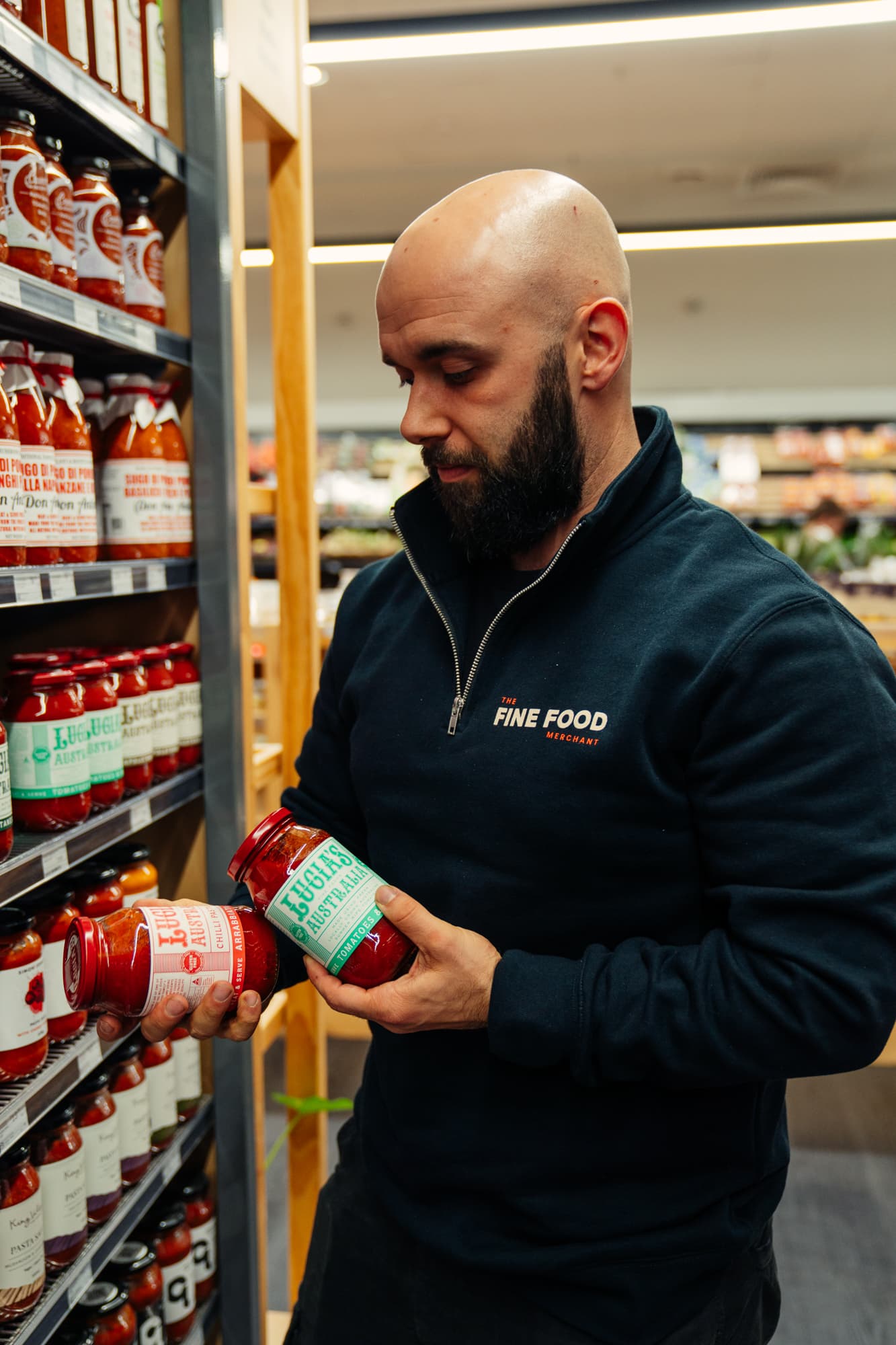 The Fine Food Merchant Owner holding jars of Lucias pasta sauces in a supermarket aisle